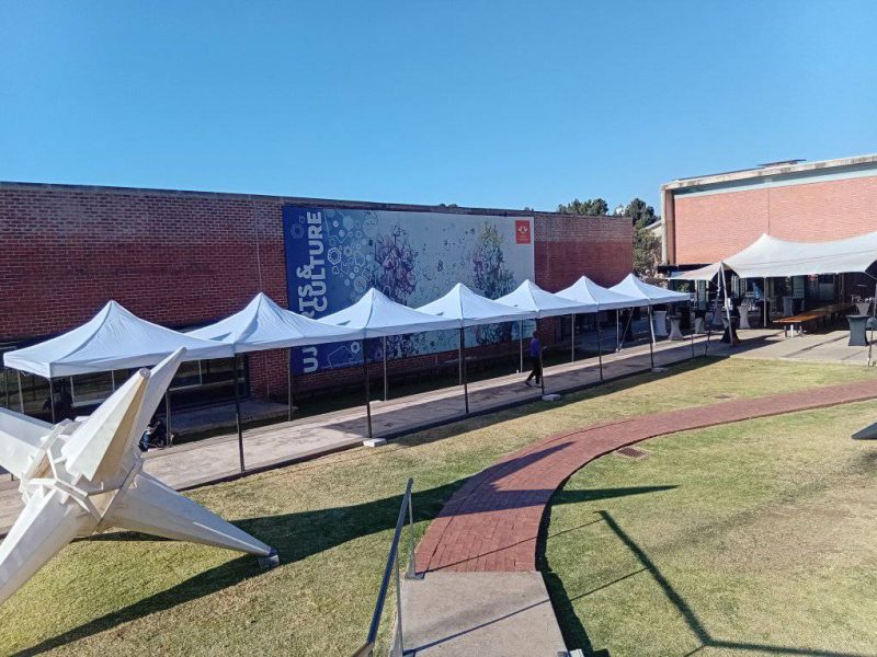 Grey stretch tent installed over an outdoor paved venue with cocktail tables and bar stools set up for a corporate cocktail event in Johannesburg