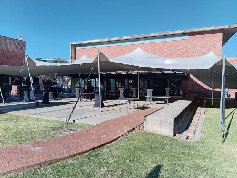 Grey stretch tent installed over an outdoor paved venue with cocktail tables and bar stools set up for a corporate cocktail event in Johannesburg